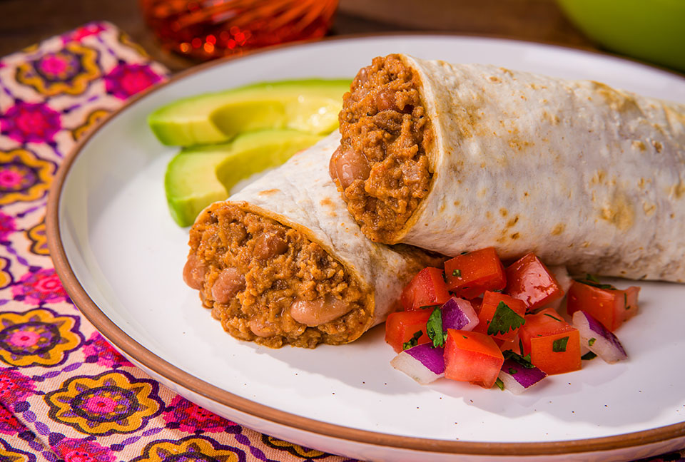 A serving of El Monterey Beef & Bean burritos, served fresh on a plate with salsa and avocado.