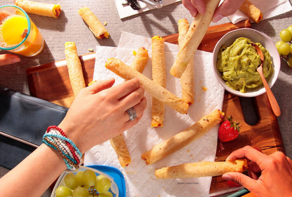 Hungry hands grabbing taquitos from a plate surrounded by dipping sauces.